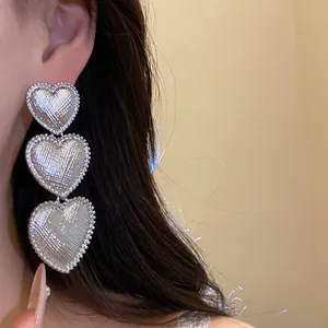 Detailed macro view of silver earrings featuring three stacked wrinkled heart charms