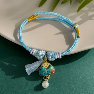 Close-up of hand-woven light blue bracelet with triangle smiley pendant and pearl charm