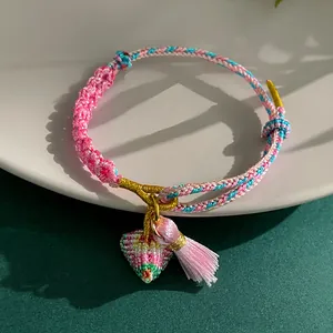 Macro view of a handmade colorful braided bracelet with a pink tassel and charm.