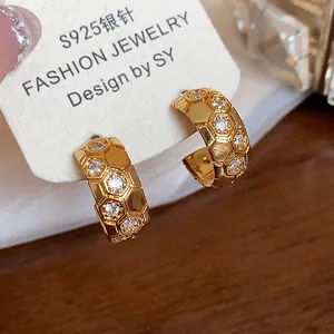 Macro detail of 18k gold plated C-shaped hoop earrings with honeycomb zircon stone pattern.