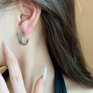 Detailed close-up of a silver C-shaped hoop earring with a honeycomb pattern