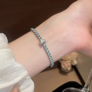 Close-up of a blue and silver braided bracelet with a sparkling charm on a woman's wrist.
