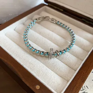 Detailed view of braided blue thread and silver link bracelet with CZ ring charm in a box
