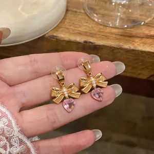 Detail view of gold bow earrings with pearls and pink heart zircon pendant