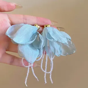 Close-up of light blue mesh flower earrings with crystal tassels and gold heart studs.