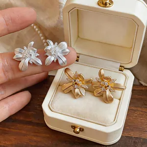 Primer plano detallado de pendientes de flores texturizadas en acabados oro y plata