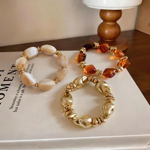 Nahaufnahme von unregelmäßigen geometrischen Perlenarmbändern in Bernstein, Weiß und Gold.