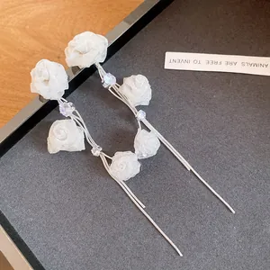 Detaillierte Makroansicht eleganter langer Quastenohrringe mit weißen Stoffrosen und Kristallen