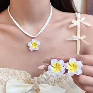 Detailopname van de witte en gele plumeria bloem hanger ketting en bijpassende oorbellen