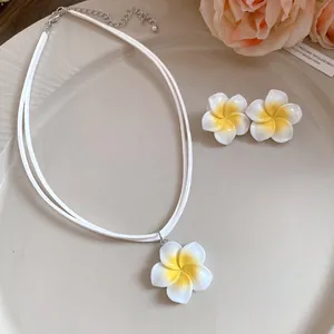Detailopname van een witte en gele plumeria bloem ketting en oorbellen set