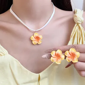 Detailopname van de Hawaiiaanse frangipani bloem hanger ketting en bijpassende oorbellen.