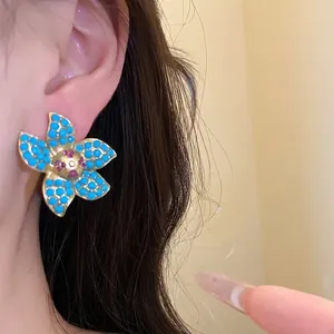 Elegant vintage gold-tone flower stud earrings with turquoise stones shown on model ear
