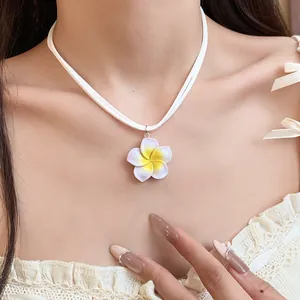 Detailopname van een geel-witte frangipani bloem hanger ketting op de nek van een model