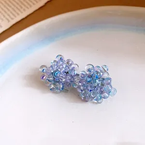 Dettaglio macro della lavorazione con perline cangianti viola e blu degli orecchini uva
