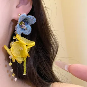 Close-up of elegant blue embroidered and yellow chiffon flower tassel earrings worn on ear