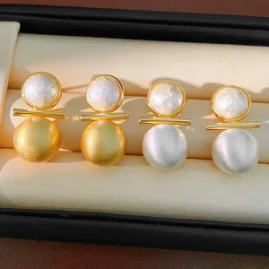 Macro detail showing the brushed gold and silver finish of stud earrings in a jewelry display box