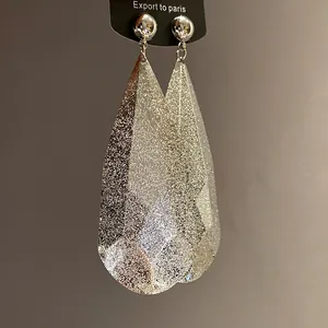 Vista dettagliata di grandi orecchini a goccia in metallo argento con finitura glitter