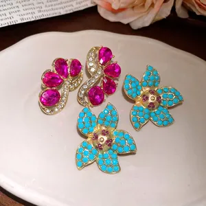 Detailed view of vintage gold flower earrings with turquoise beads and pink gems on a plate.