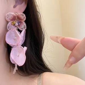 Macro detail of sweet pink chiffon flower tassel earrings with silver needles worn on ear
