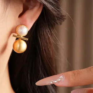 Close-up of brushed gold spherical earring with pearl inlay worn on a model's ear