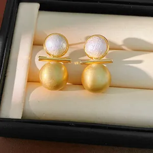 Detailed close-up showing texture of pearl and brushed gold spherical drop earrings