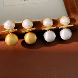 Close-up of elegant brushed gold and silver pearl earrings displayed on a brown leather stand