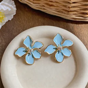 Primo piano di orecchini a lobo a fiore in smalto blu con bordo dorato e cristalli