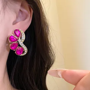 Close-up of vintage gold-tone earrings with fuchsia teardrop stones and white crystals.