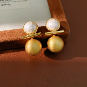 Macro detail of brushed gold sphere and white pearl geometric stud earrings on velvet