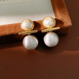 Detailed macro view of gold-plated brushed silver ball and round pearl stud earrings.