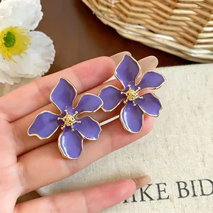 Primo piano di eleganti orecchini a lobo a fiore in smalto viola con bordi dorati estivi
