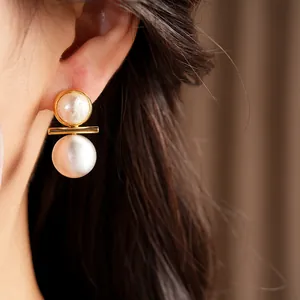 Detail shot of elegant brushed silver pearl stud earrings with gold plating worn on ear