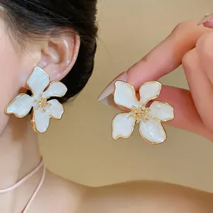 Eleganti orecchini a lobo a forma di fiore in smalto bianco con bordo dorato sull'orecchio.