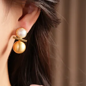 Close-up shot of an elegant gold-plated earring with a brushed metal sphere and pearl