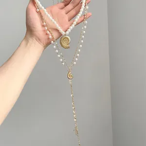 Macro detail of elegant layered pearl necklace featuring golden conch and cross pendants