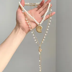 Close-up detail of a layered gold chain necklace featuring white pearls and conch shell pendants