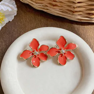 Dettaglio di orecchini a lobo a forma di fiore in smalto arancione con bordo dorato