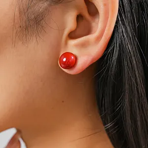 Detailed macro view of a elegant shiny red round pearl stud earring worn on a human ear model.