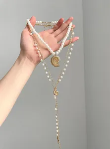 Detailed macro view of layered necklace with pearls and golden shell pendants in hand