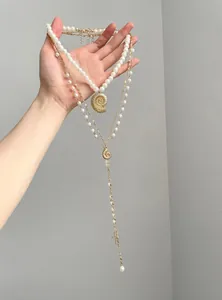 Detailed view of layered necklace with gold conch shell, pearls and cross pendant.