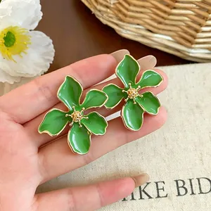 Primo piano di orecchini a lobo a forma di fiore in smalto verde con stami dorati