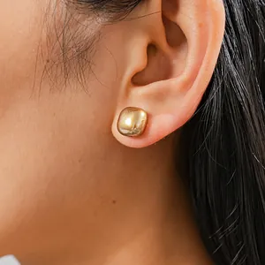 Close-up view of a minimalist gold square rounded stud earring worn on an ear