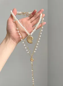 Detailed view of a golden layered necklace with shell pendants and elegant faux pearls.