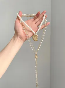 Detailed view of layered white pearl necklaces featuring golden conch shell pendants