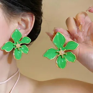 Primo piano di orecchini a lobo a forma di fiore in smalto verde con bordi dorati.