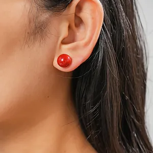 Close-up detail of a minimalist glossy red round stud earring worn on a model's ear