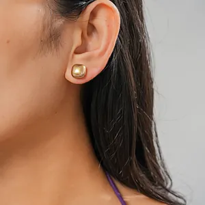 Close-up detail of a minimalist gold square stud earring worn on model's ear.