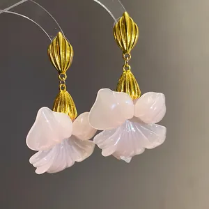 Macro detail of elegant pink resin flower petals and golden leaf accents of these earrings