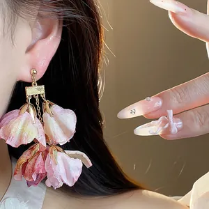 Nahaufnahme von eleganten rosa Stoffblumen-Ohrringen getragen von einem Modell bei Licht.