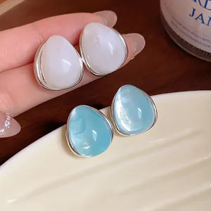 Vista macro de pendientes de gota de acrílico azul y blanco con borde plateado